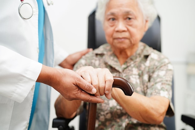 Dokter helpt Aziatische oudere handicap vrouw patiënt met wandelstok in gerimpelde hand