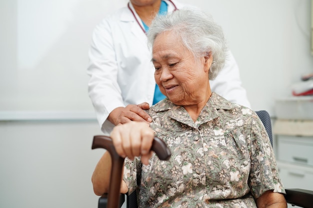 Dokter helpt Aziatische oudere invaliditeit vrouw patiënt met wandelstok in gerimpelde hand in het ziekenhuis