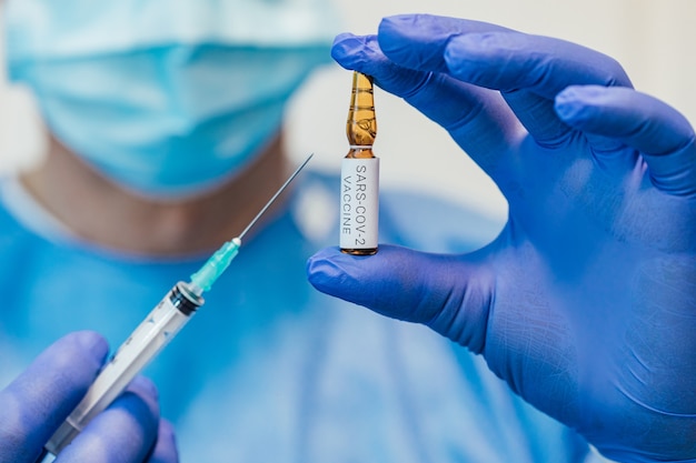 Dokter houdt een spuit met een naald in de ene hand en een container met het COVID-19-vaccin in de andere.