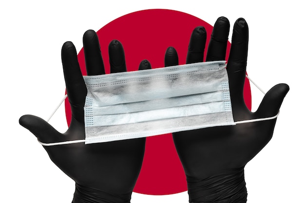 Dokter houdt gezichtsmasker in handen in zwarte medische handschoenen op achtergrondkleuren vlag van vlag van japan o...