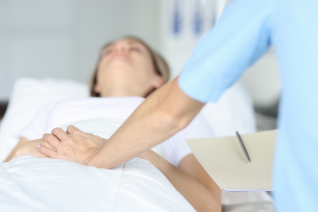 Dokter houdt liggende patiënt met de hand op ziekenhuisbed. Intramuraal onderzoek concept