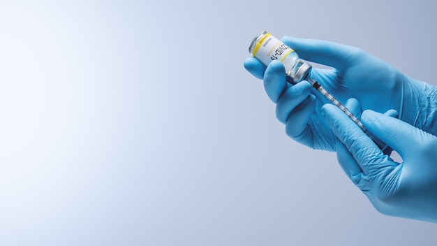 Dokter in blauwe latexhandschoenen vult spuit in met vaccin uit glazen injectieflacon