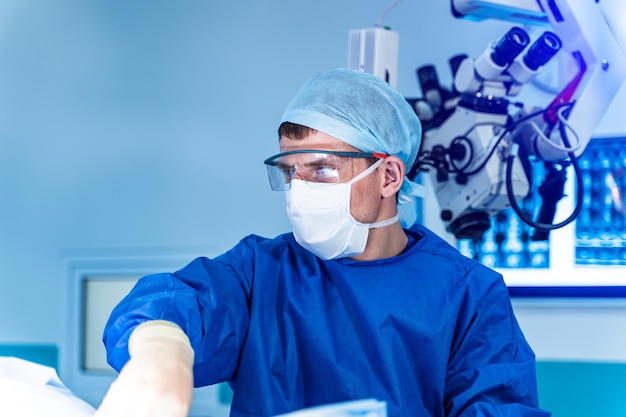 Dokter in blauwe scrubs biedt neurochirurgische operaties. Moderne apparatuur met chirurgie Microscoop op de achtergrond. Selectieve aandacht. Detailopname.