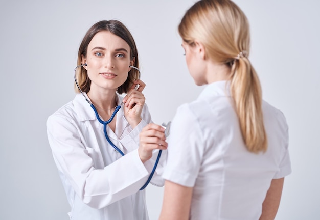 Dokter in een medisch gewaad op een lichte achtergrond en een blonde vrouwelijke patiënt Hoogwaardige foto