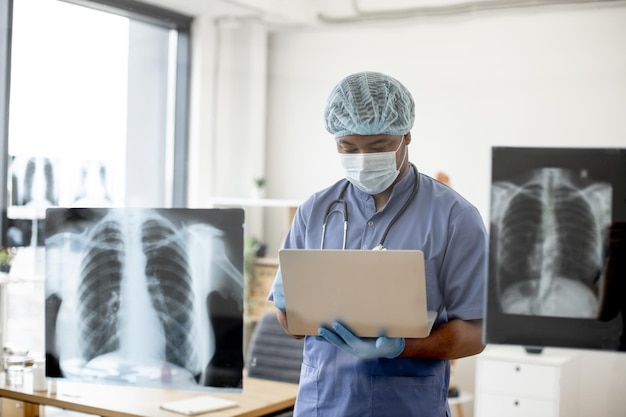 Dokter in masker en scrubs onderzoekt röntgenscans via laptop