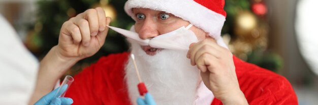 Dokter in rubberen handschoenen die een neusuitstrijkje van pcr neemt voor de kerstman bij de kerstboom