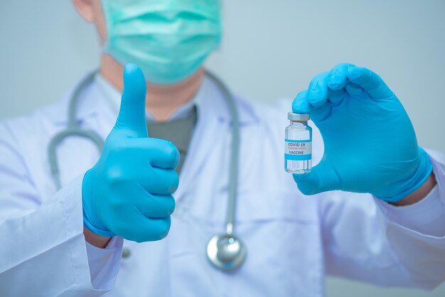 Dokter in uniform met stethoscoop houdt vaccinatie Coronavirus vast en duimen omhoog