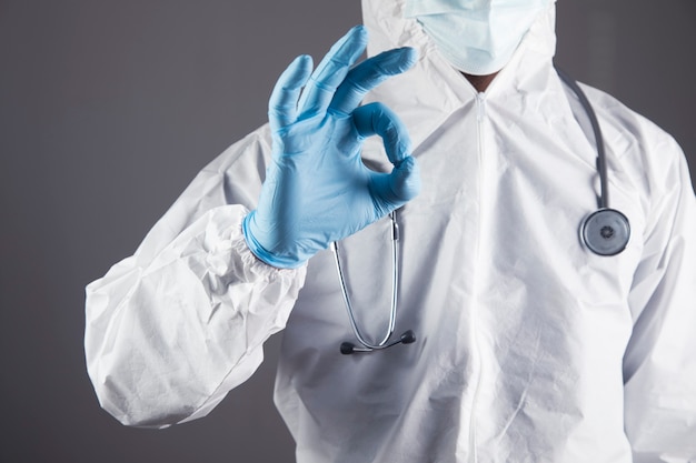 Dokter in wit beschermend uniform toont ok op een grijze scène