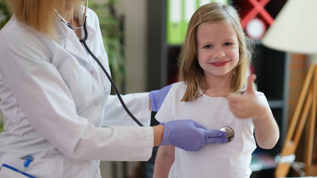 Dokter luistert naar kind met stethoscoop meisje houdt duimen omhoog