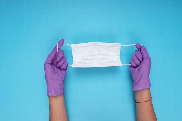 Dokter met een wit chirurgisch masker en een paar lila handschoenen op een lichtblauwe achtergrond