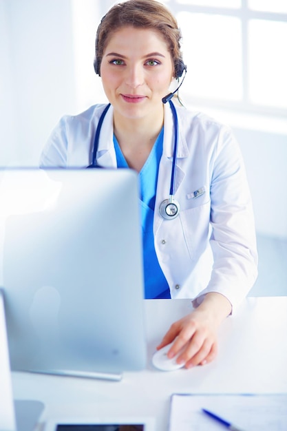 Dokter met headset zit achter een bureau met laptop