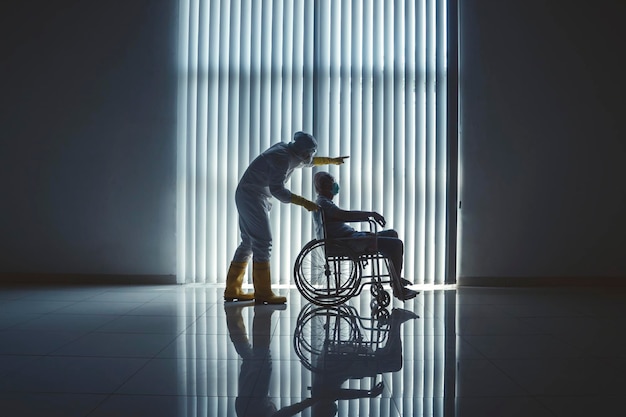 Dokter met pak voor gevaarlijke stoffen die een oudere patiënt in een rolstoel duwt