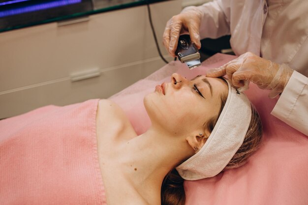 Dokter met ultrasone schraper Procedure voor ultrasone reiniging van gezicht Modelprofiel Cosmetologische kliniek Patiënt Gezondheidszorg kliniek cosmetologie