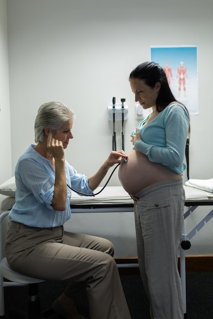 Dokter onderzoekt de buik van een zwangere vrouw met een stethoscoop in de onderzoekskamer