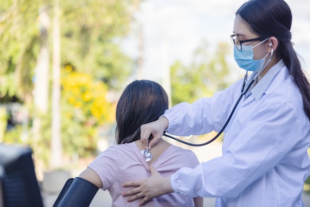 Dokter onderzoekt een vrouwelijke patiënt met een stethoscoop in een zomerpark.
