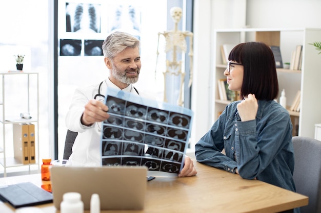 Dokter onderzoekt MRI-scans terwijl vrouw aan bureau zit