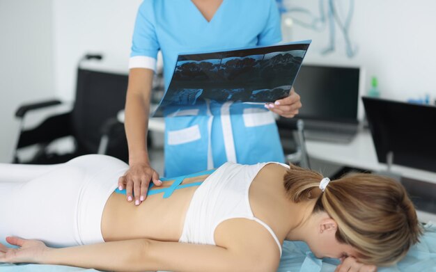 Dokter onderzoekt röntgen van vrouwen terug zetten kinesiologie tape op pijnlijke deel van het lichaam