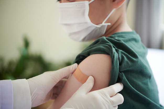 Dokter plakt pleister over covid-vaccininjectieplaats op arm van preteenjongen in medische ...