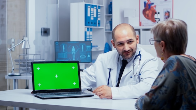 Dokter praat in de buurt van een laptop met groen scherm en oudere patiënt die ernaar kijkt. mockup mock-up geïsoleerde achtergrond klaar om te worden verwijderd chromakey keying voor uw app of advertentie