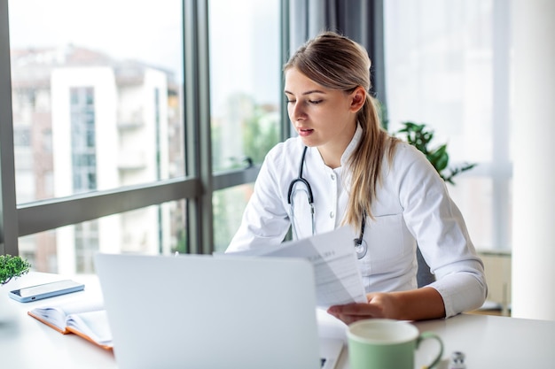 Dokter professionele vrouwelijke arts in uniform die aantekeningen maakt in medisch dagboek en documenten vult ziektegeschiedenis van de patiënt kijken naar laptop scherm student kijken naar webinar