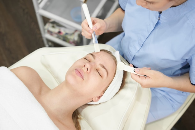 Foto dokter schoonheidsspecialist maakt gezichtsreinigingsprocedure voor jonge vrouw in de schoonheidssalon, huidverzorging