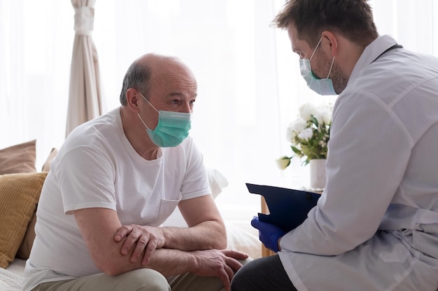 Dokter schrijft medisch recept aan oudere man die hem thuis bezoekt