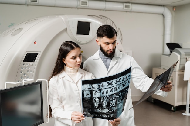 Dokter-stagiair meisje studeert in de CT-computertomografiescankamer bij stagecursussen Collega-artsen bespreken röntgenfoto's in de CT-computertomografiescankamer