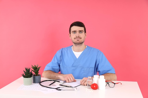 Dokter stagiair zit op de werkplek op roze achtergrond