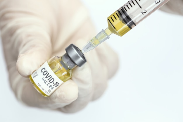 Dokter, verpleegster, wetenschapper hand draagt medische handschoen met spuit en flesje met COVID-19 coronavirusvaccin voor injecties. Vaccin tegen COVID-19 coronavirus, gezondheidszorg en medisch concept.