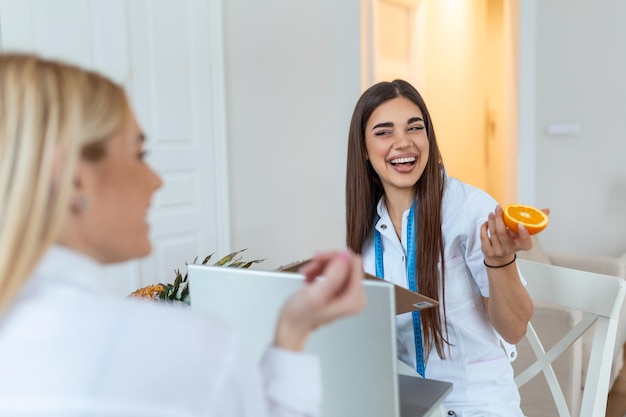 Dokter voedingsdeskundige diëtist en vrouwelijke patiënt op consultatie in het kantoor jonge glimlachende vrouwelijke voedingsdeskundige in de spreekkamer voedingsdeskundige bureau met gezond fruit en meetlint