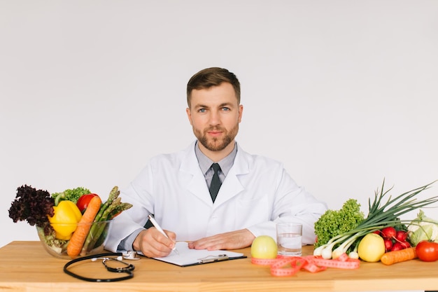 Dokter voedingsdeskundige zittend op de werkplek aan de balie in kantoor onder verse groenten dieetplan concept