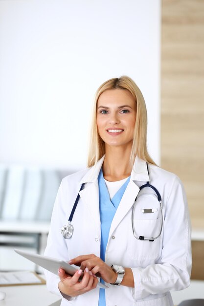 Foto dokter vrouw aan het werk in het ziekenhuis opgewonden en blij met haar beroep blonde arts controleert medicatiegeschiedenisrecords en examenresultaten tijdens het gebruik van tabletcomputer geneeskunde en gezondheidszorgconcept