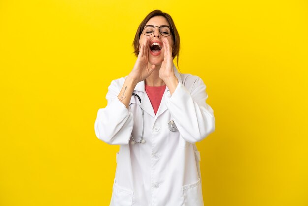 Dokter vrouw geïsoleerd op gele achtergrond schreeuwen en iets aankondigen