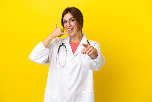 Dokter vrouw geïsoleerd op gele achtergrond telefoon gebaar maken en naar voren wijzen