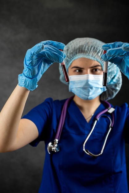 Dokter vrouw in blauw uniform kijk bloedmonster in testbuis geïsoleerd op zwart Bloedanalyse covid-19