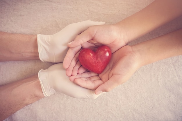 Dokterhanden met handschoenen die kindhanden, rood hart, ziektekostenverzekering, schenkingconcept houden