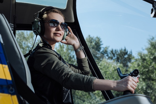 Dol op vliegen. De close up van een charmante jonge vrouw, zittend in de pilootcabine van een helikopter en poseren voor de camera