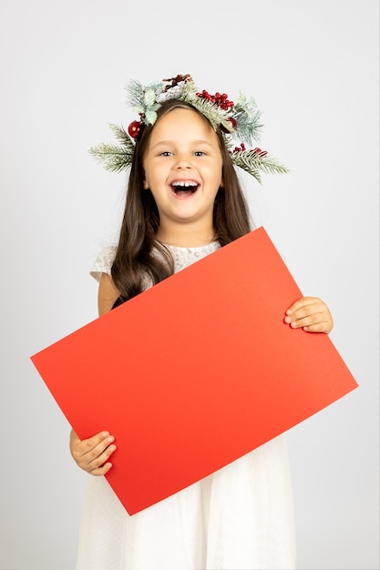 Dolblij gelukkige meisjes in een kerstkrans met een rood blanco papier met kopie ruimte geïsoleerd op een ...