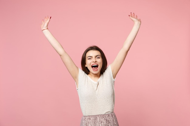 Dolblij jong meisje in casual lichte kleding poseren geïsoleerd op pastel roze achtergrond studio portret. Mensen oprechte emoties levensstijl concept. Bespotten kopie ruimte. Stijgende spreidende handen schreeuwen.