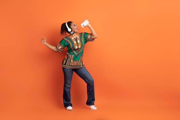 Dolblije afrikaanse vrouw die karaoke zingt met koptelefoon en smartphone