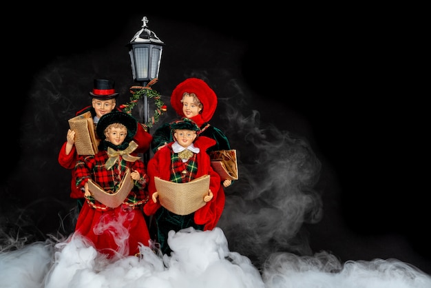 Doll family singing Christmas carols in the night with misty smoke.