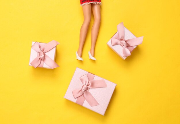 Doll feet and gift boxes on a yellow background Minimalism