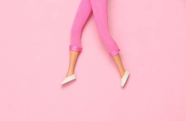 Doll female legs on pink background Creative minimalistic layout