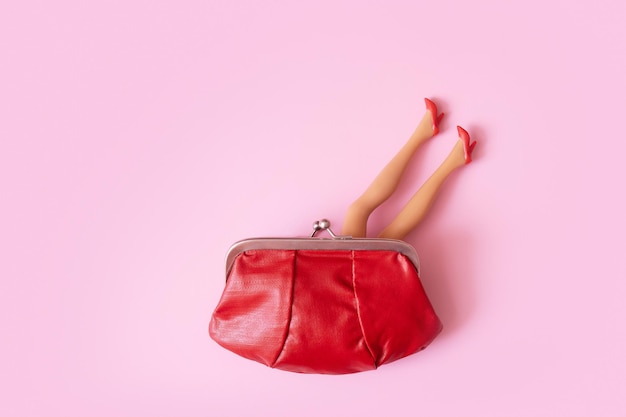 Doll legs in red shoes sticking out of the purse top view Creative female shopping or finanse concept