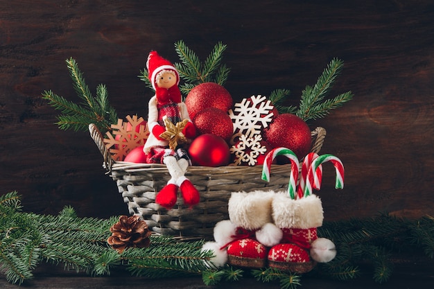 Doll sitting in a basket with fir tree branches, red balls and s