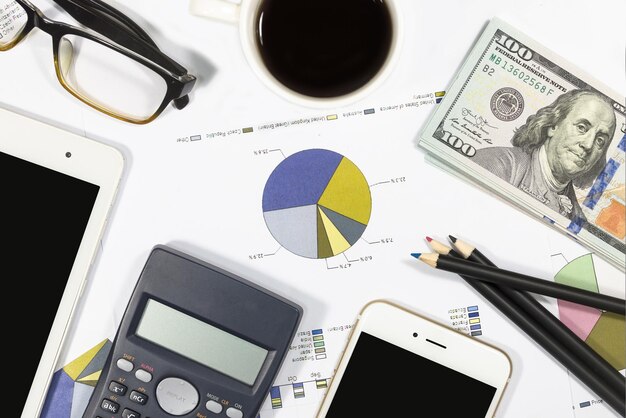 Калькулятор долларовых банкнот, ручка, кофейные очки, планшет, мобильный телефон и бизнес-графики лежат на столе