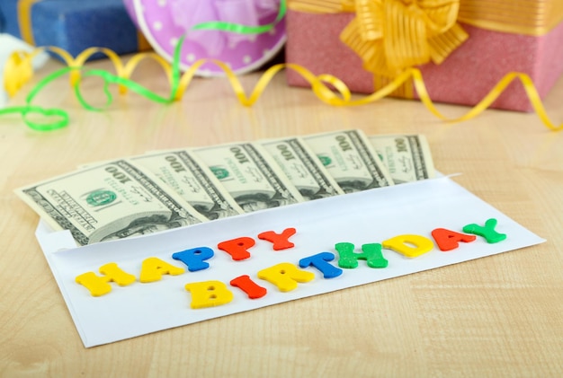 Dollar bills in envelope as gift at birthday on wooden table closeup