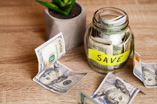 Dollar bills in glass jar and text save on wooden table