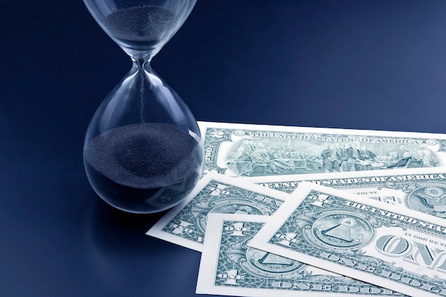 Dollar bills lie near the hourglass. Time is money