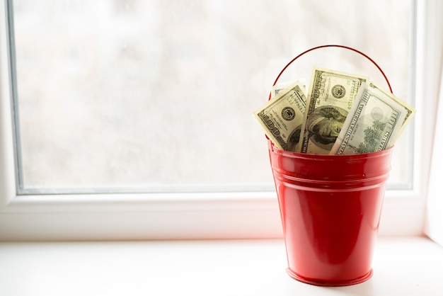 Dollar bills in red pail. on white window.light background. 